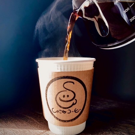 しゃこねコーヒーのイメージ画像。店舗ロゴが描かれた紙製のスリーブがついたコップにコーヒーが注がれている写真